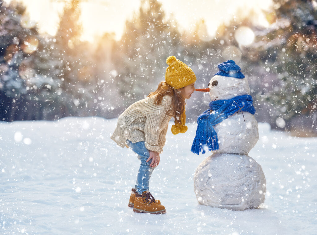 happy child girl playing with a snowman on a snowy winter walk