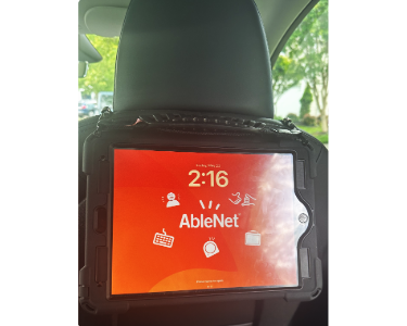 A QuickTalker Freestyle attached to the back of a car seat headrest.