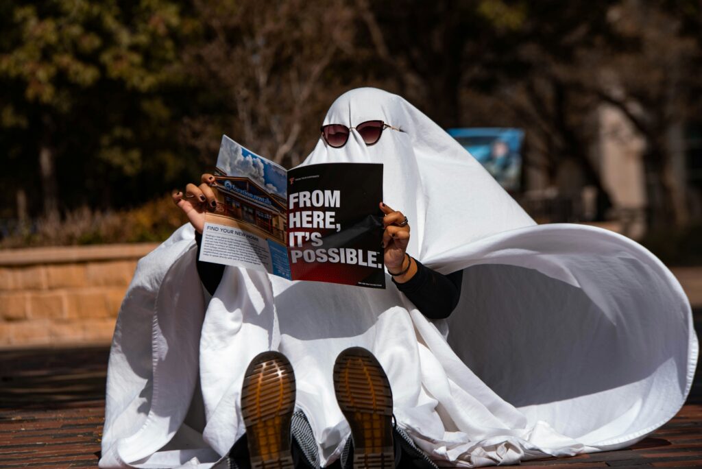Person Dressed as a ghost reading outdoors on a bench